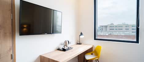 Una habitación moderna con un escritorio de madera, una silla amarilla, un televisor de pantalla plana y una ventana con vista a la ciudad.