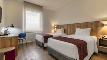 A hotel room with two beds, a desk, a chair, and a window.