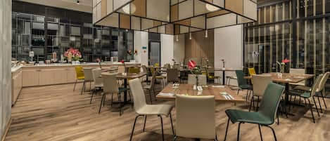 A modern dining area with wooden flooring, multiple tables and chairs, and large windows providing natural light.