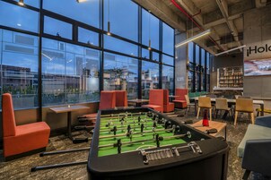 Una mesa de fútbolín en un área de estar moderna con ventanas amplias, asientos cómodos y una barra visible.