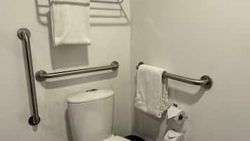 Un baño pequeño y moderno con inodoro blanco, barras de apoyo, toallero y porta papel.