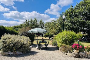 Un jardin avec une table et des chaises, un espace salon abrité et diverses plantes.