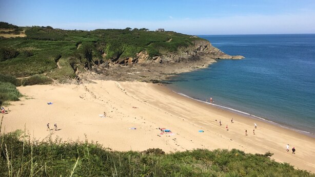 A sandy beach with people walking and some umbrellas.