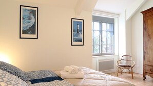A bedroom with a bed, a chair, a wardrobe, and two framed pictures on the wall.