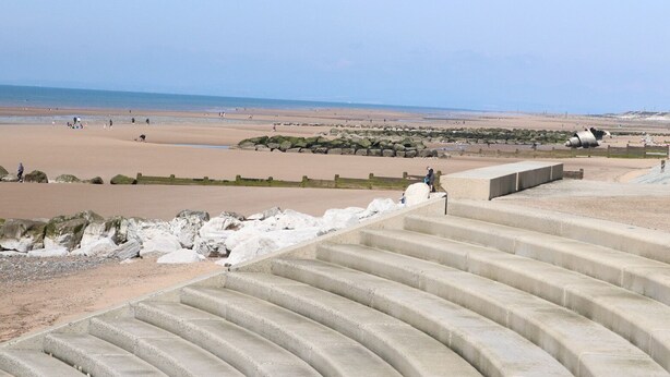 Een strand met betonnen trappen die naar het strand leiden, zand en een heldere lucht.