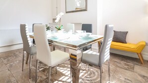 Een eetgedeelte met een glazen tafel, vier stoelen, een gele bank en een spiegel aan de muur.