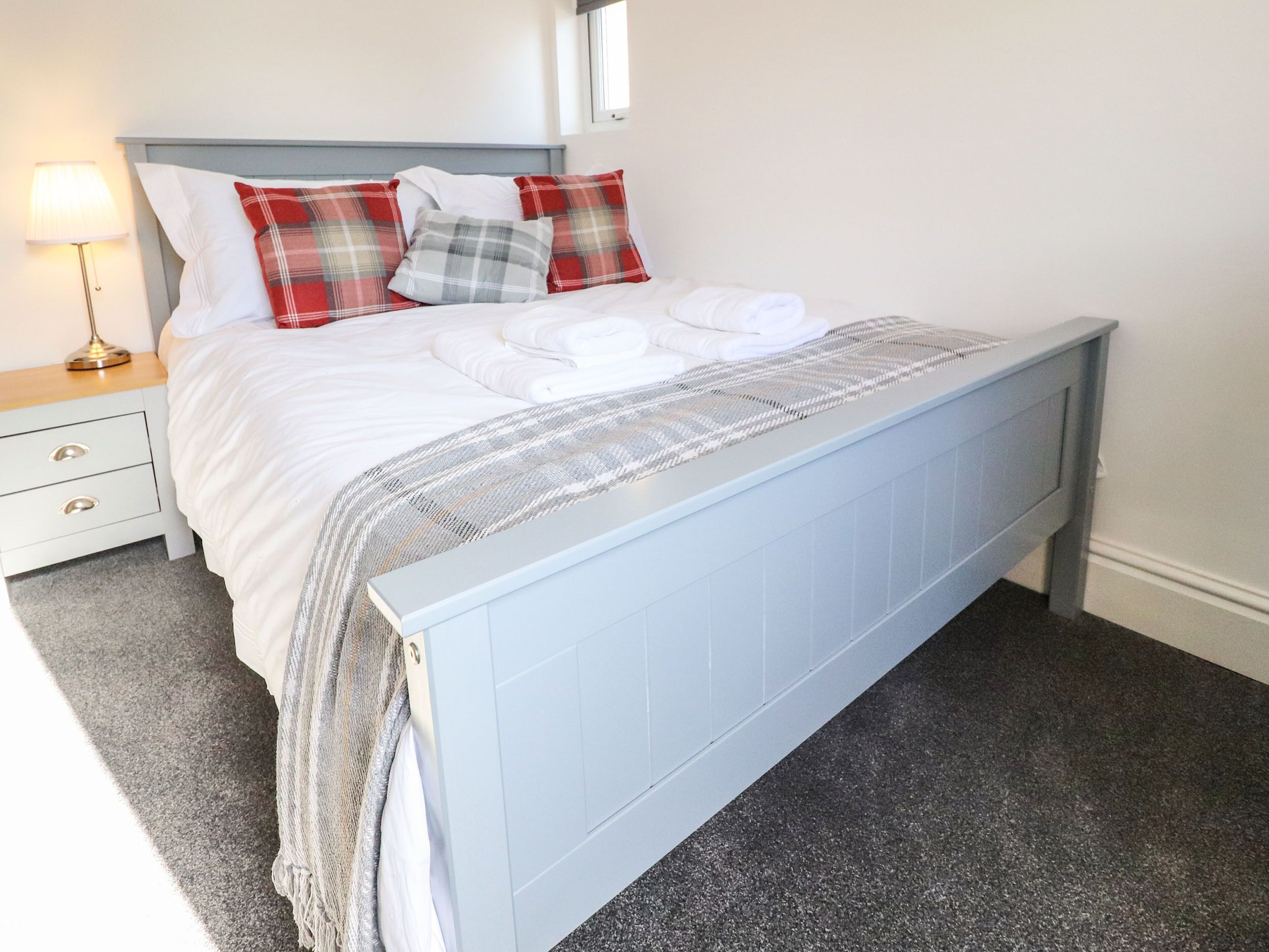 Un lit bien fait, avec une literie blanche, des coussins à carreaux et un plaid gris.