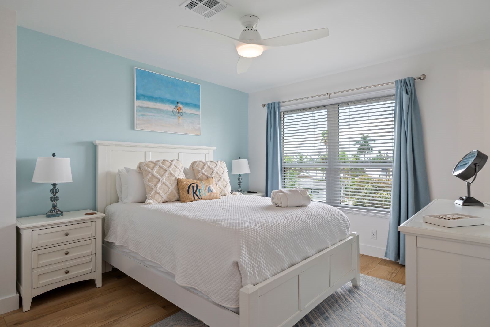 A bedroom with a bed, nightstands, a desk, a ceiling fan, and a window with curtains.