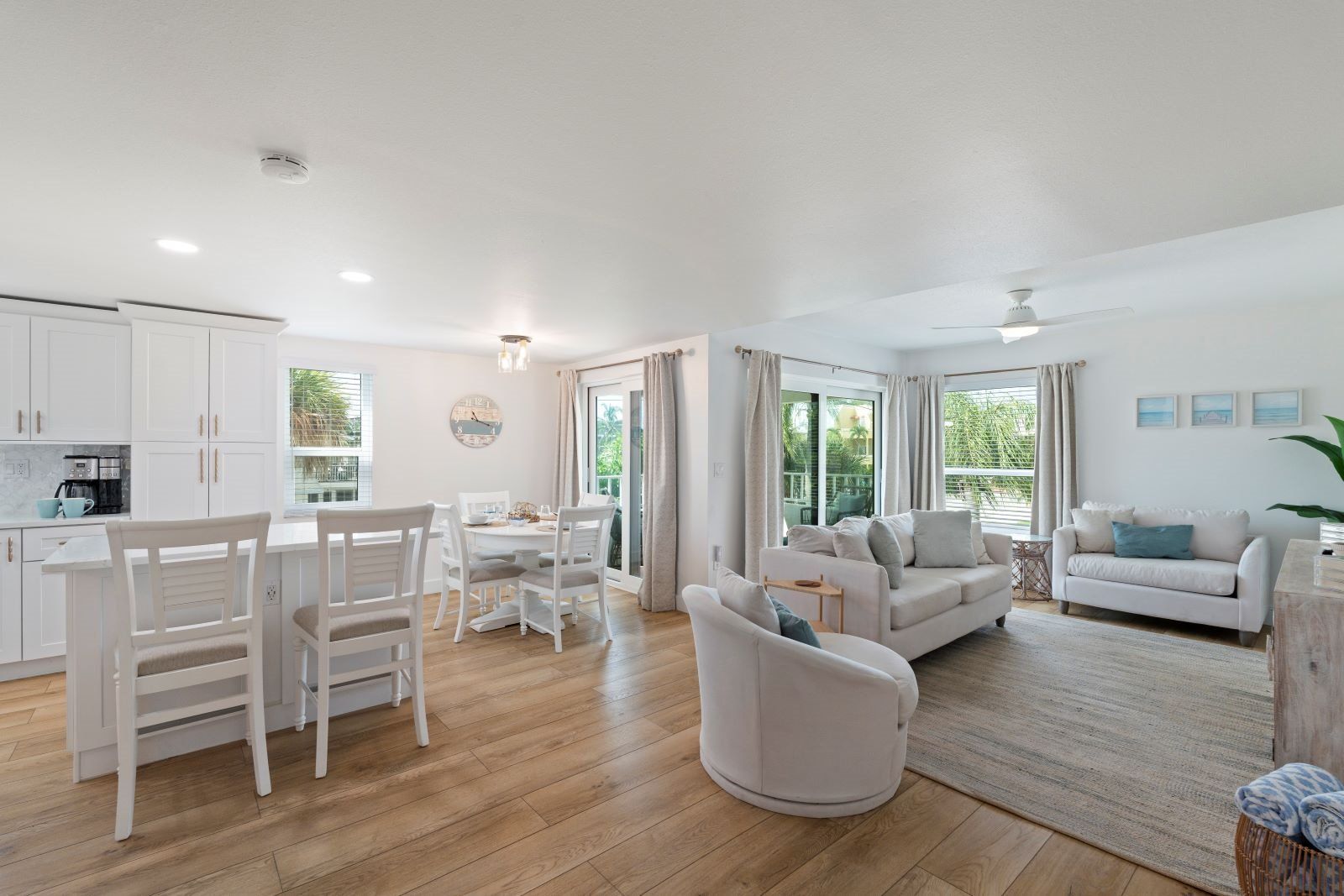 A spacious living area with a dining table, white furniture, and a large window.