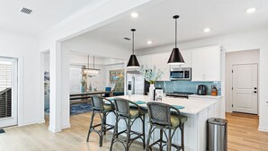 Une cuisine moderne dotée d’un îlot central, de tabourets de bar, de luminaires suspendus et d’une poubelle en acier inoxydable.