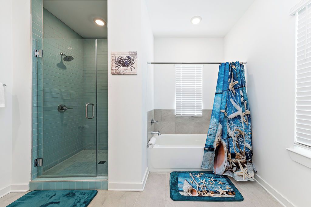 A bathroom with a glass-enclosed shower, a bathtub, and a shower curtain with a nautical theme.