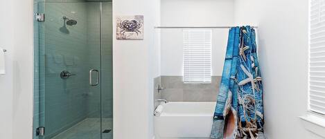 A bathroom with a glass-enclosed shower, a bathtub, and a shower curtain with a nautical theme.