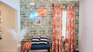 Une pièce avec un lit, un néon, un mur à la texture bois et des rideaux orange.