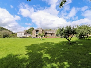 Une maison en pierre avec une grande pelouse et un arbre au premier plan.