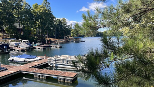 A marina with boats docked at wooden piers, surrounded by trees and a calm lake.