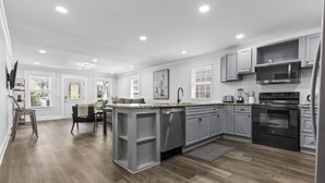 Une cuisine moderne avec des meubles gris, un îlot central, des appareils en acier inoxydable et un plancher en bois.