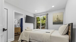 Une chambre à coucher avec un lit, un téléviseur fixé au mur, un tableau et une vue sur l’extérieur.