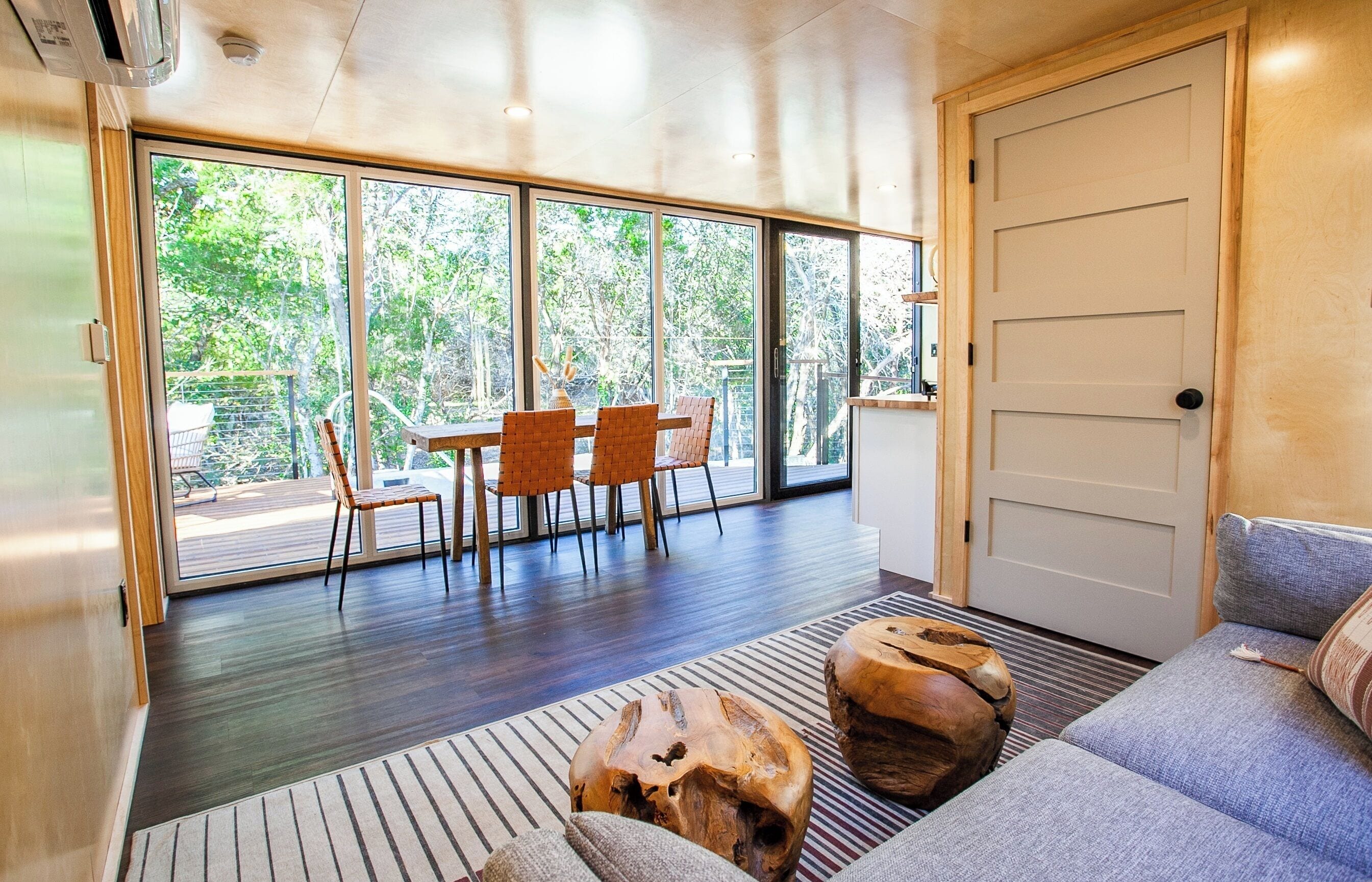 A modern interior with a dining area, large windows, and a wooden door.