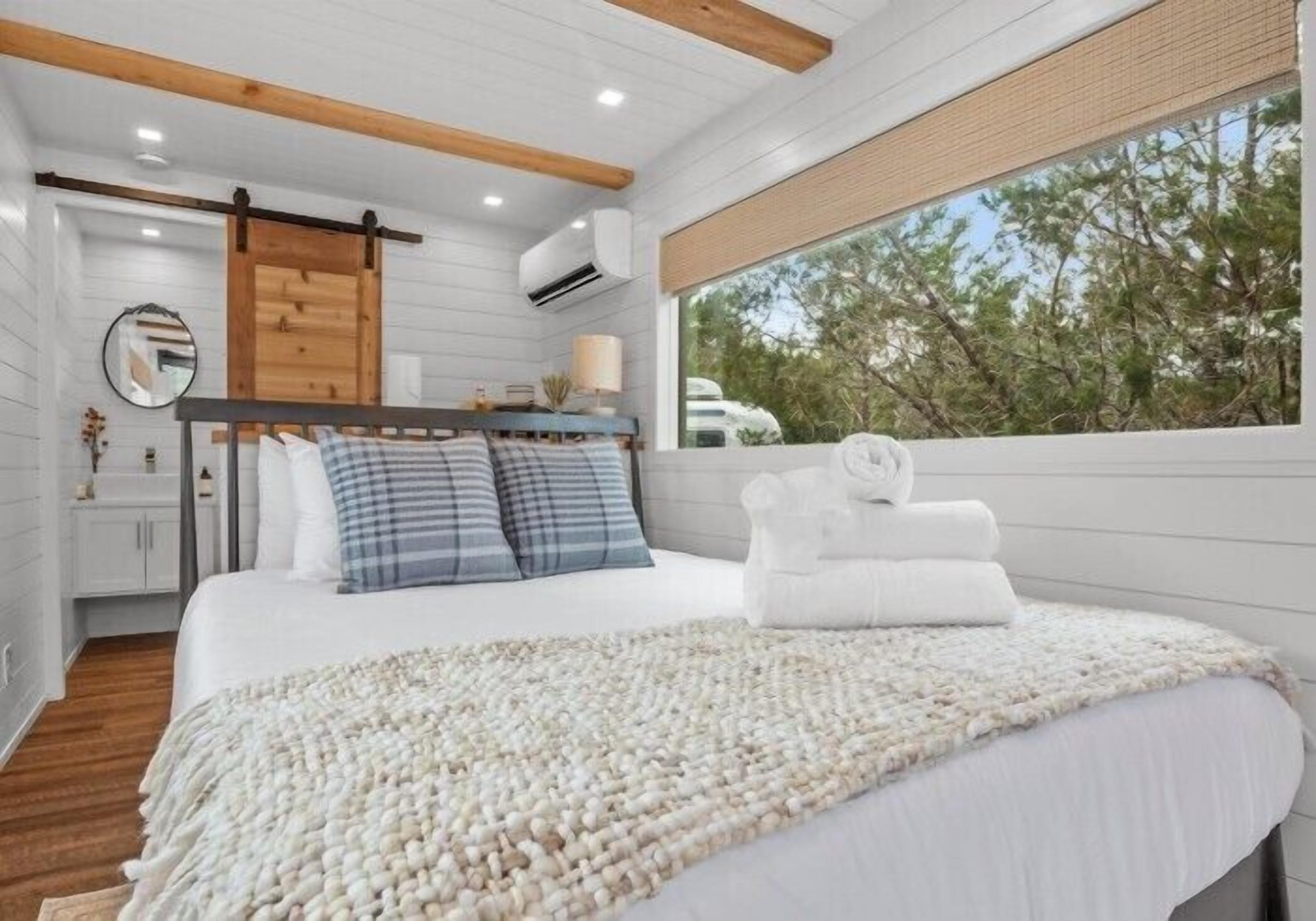 Une chambre à coucher avec un lit, un plafond en bois, une fenêtre et une vue sur les arbres.