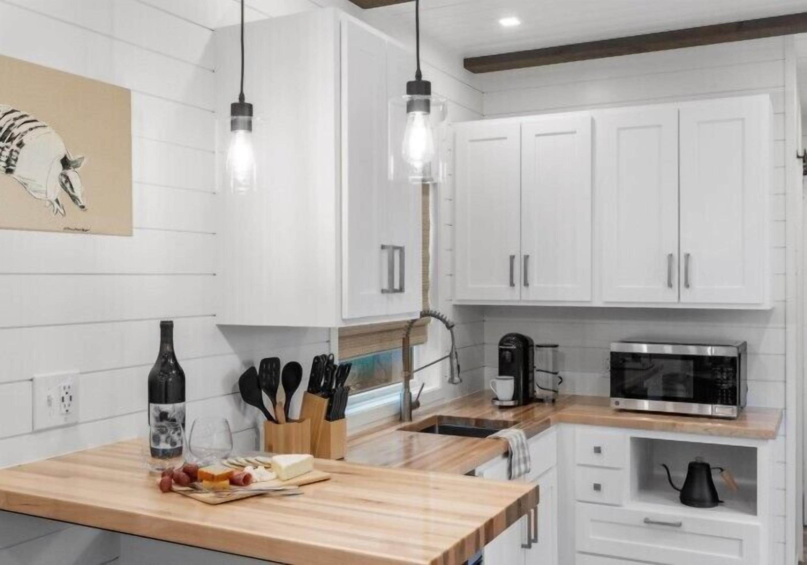 A modern kitchen with white cabinets, a wooden countertop, a wine bottle, and a coffee maker.