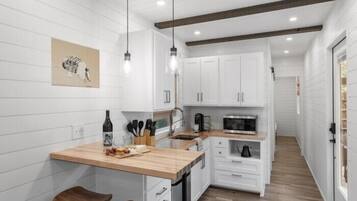 A modern kitchen with white cabinetry, a wooden countertop, and pendant lighting.