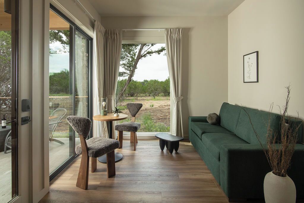 A modern living room with a green sofa, two chairs, a small round table, and a vase with branches.