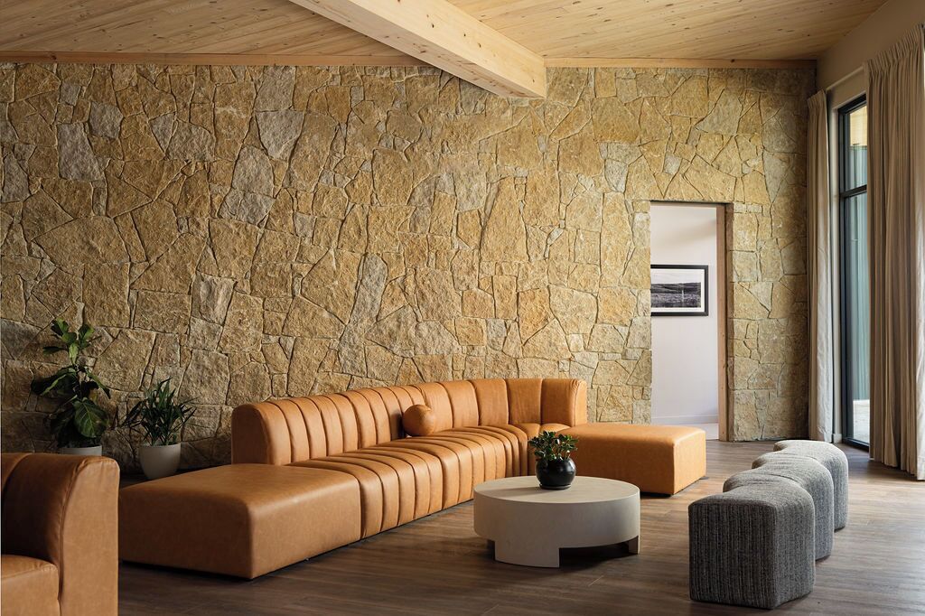 Uma sala de estar moderna com uma parede de pedra, um sofá de couro, uma mesa de centro redonda e uma pequena planta.