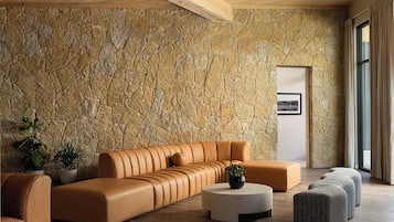 Uma sala de estar moderna com uma parede de pedra, um sofá de couro, uma mesa de centro redonda e uma pequena planta.