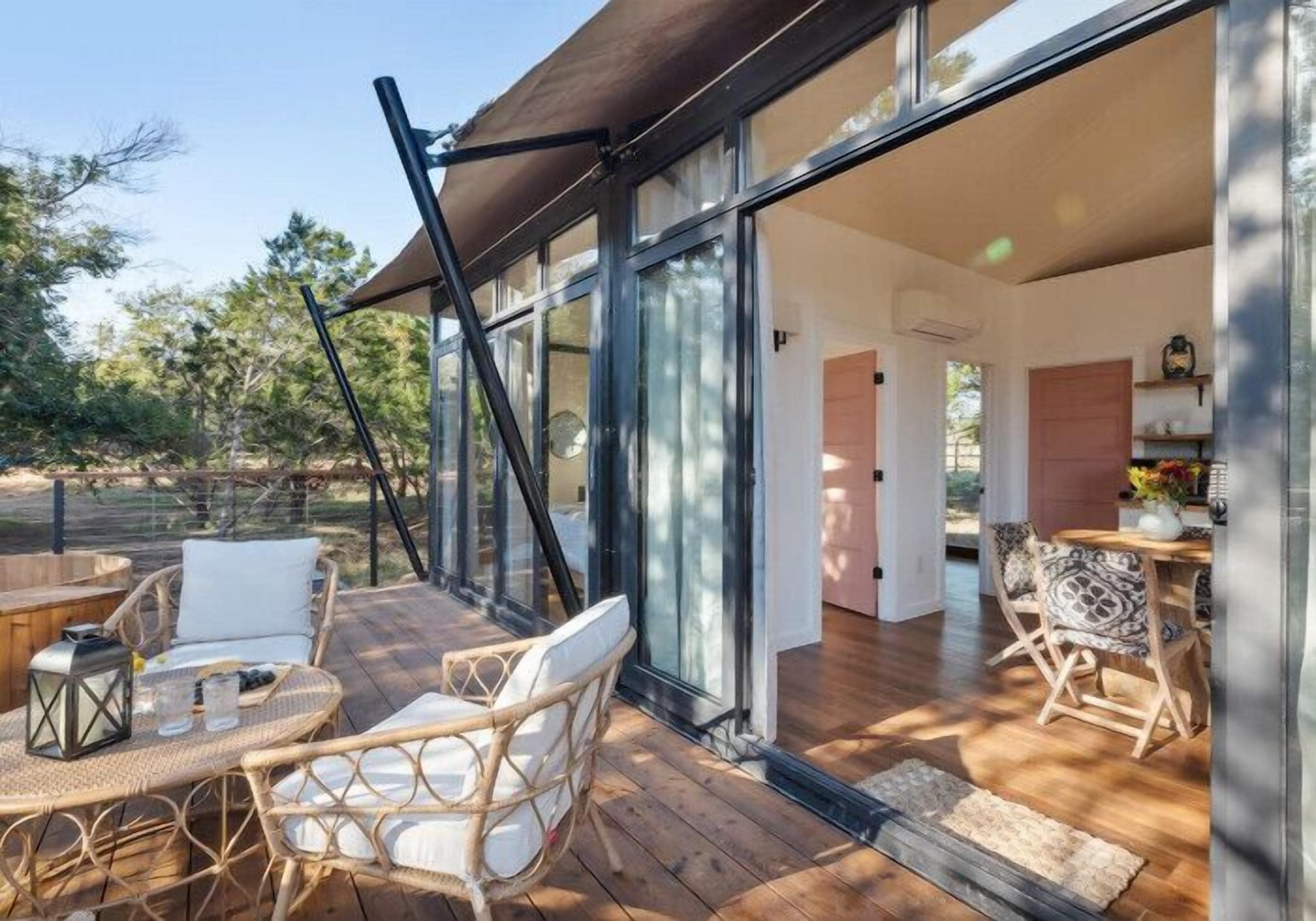 Un patio moderno al aire libre con mobiliario de mimbre y un ventanal de vidrio que da a una habitación con piso de madera y zona de comedor.