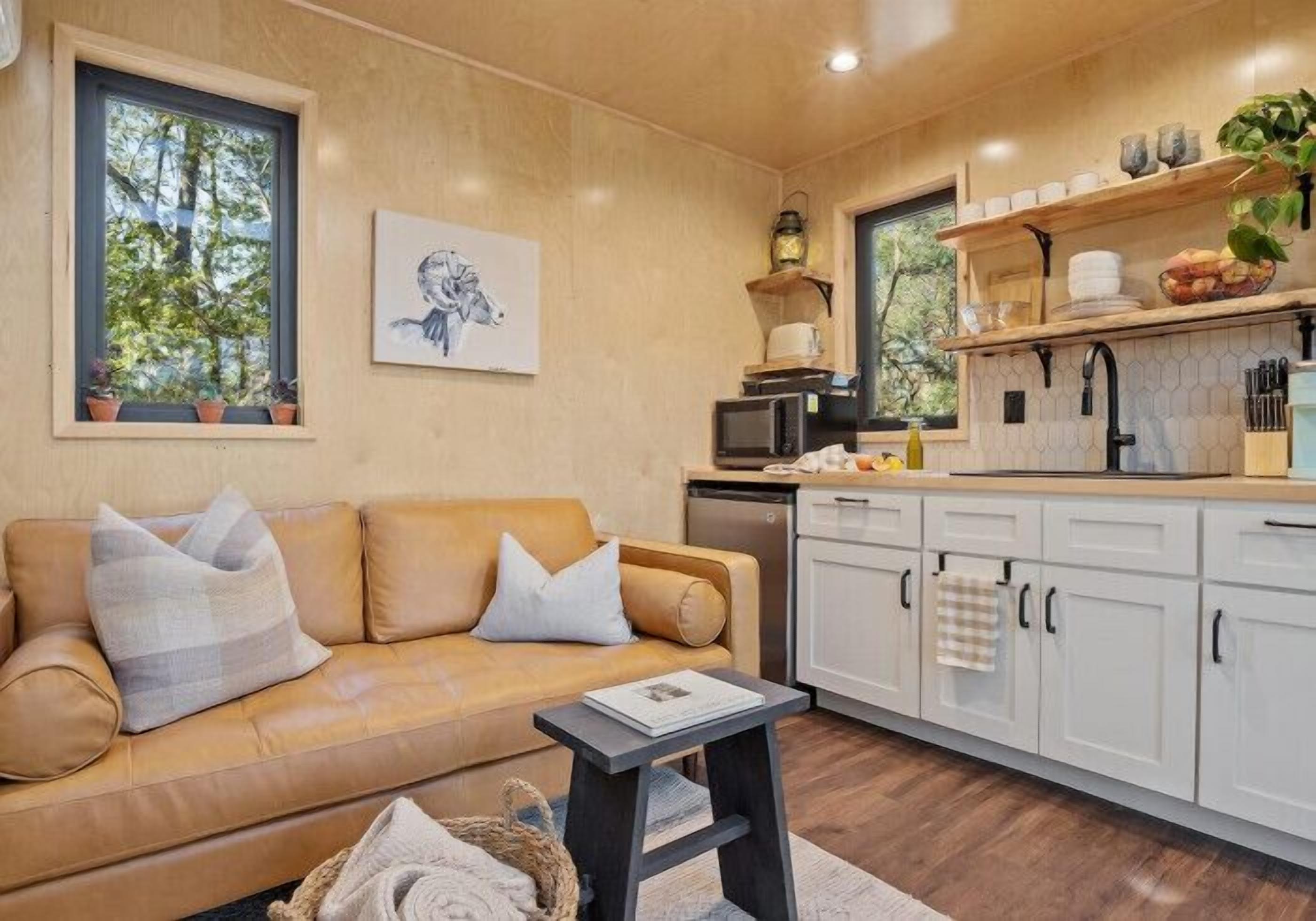 A cozy living room with a sofa, a small table, and a kitchen area with white cabinets and a microwave.