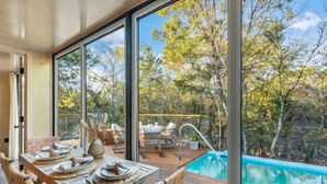 Un coin repas avec une table dressée pour deux personnes, donnant sur une piscine et un paysage naturel.