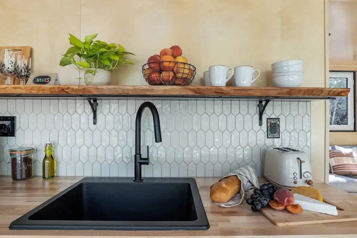 A kitchen with a black sink, a white tiled backsplash, a wooden countertop, a toaster, and a fruit bowl.