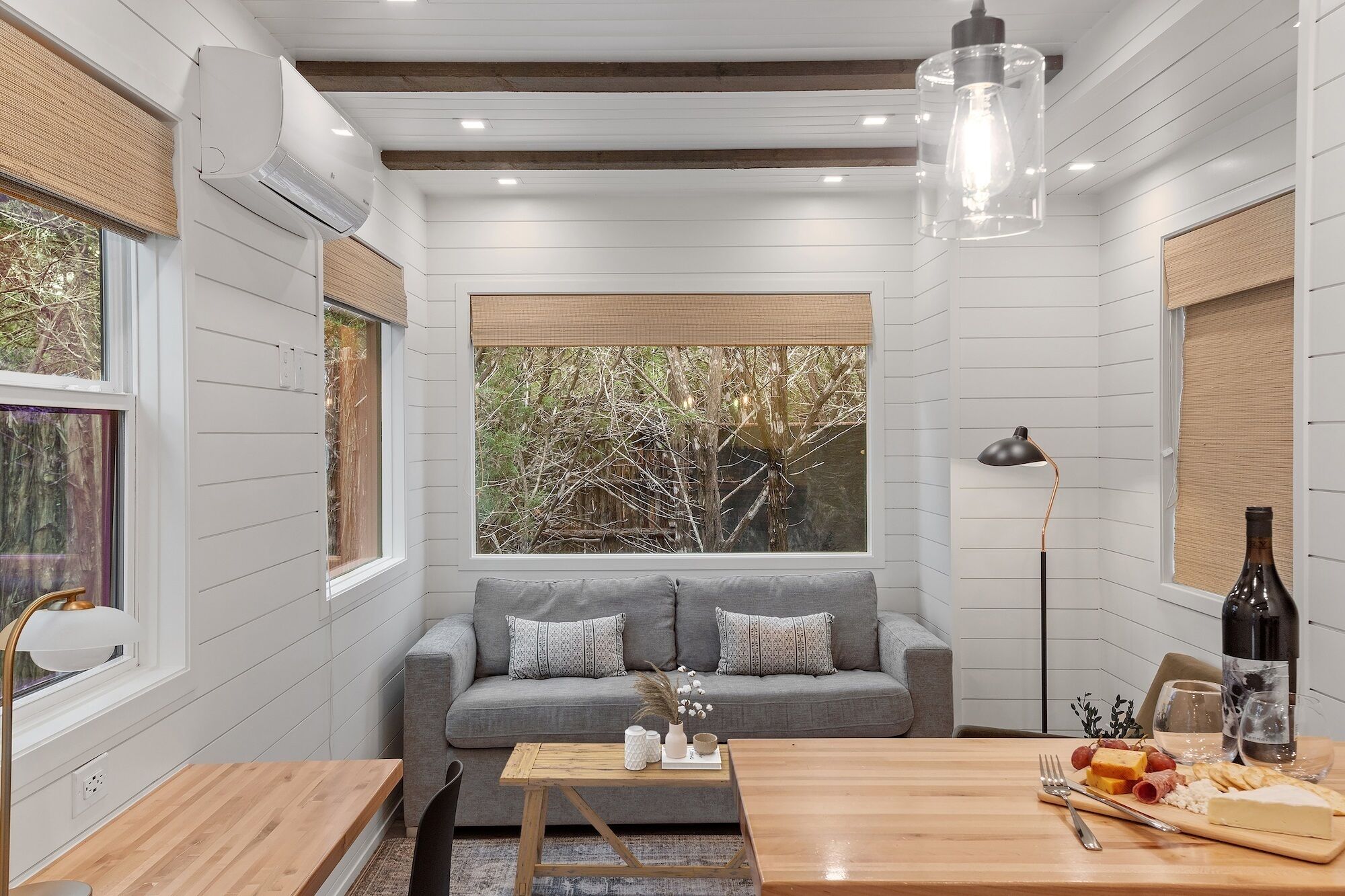 A cozy living room with a grey sofa, wooden coffee table, and a dining table set with food and drinks.