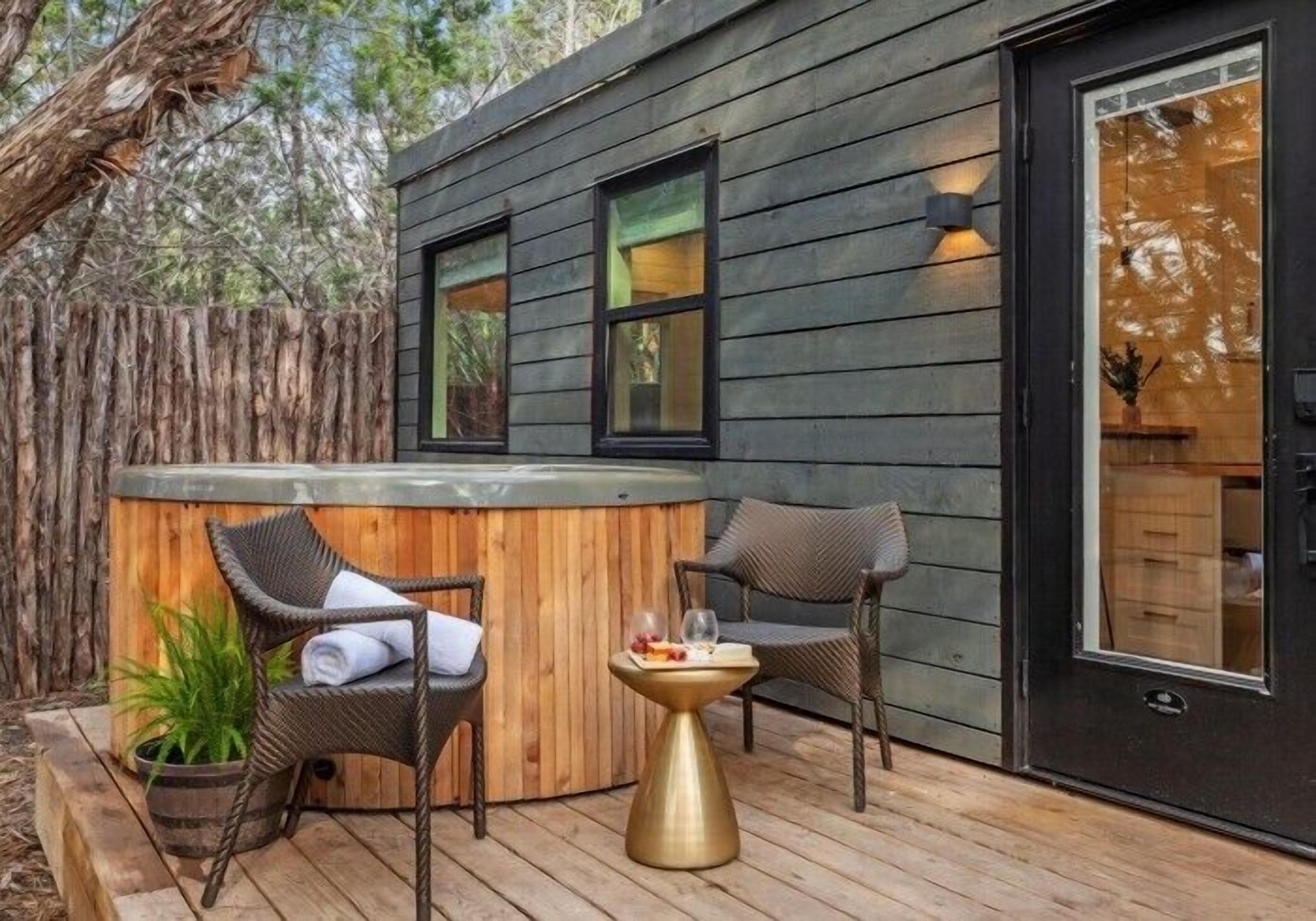 Una terraza de madera con un jacuzzi, sillas de mimbre y una mesita con vasos y fruta.