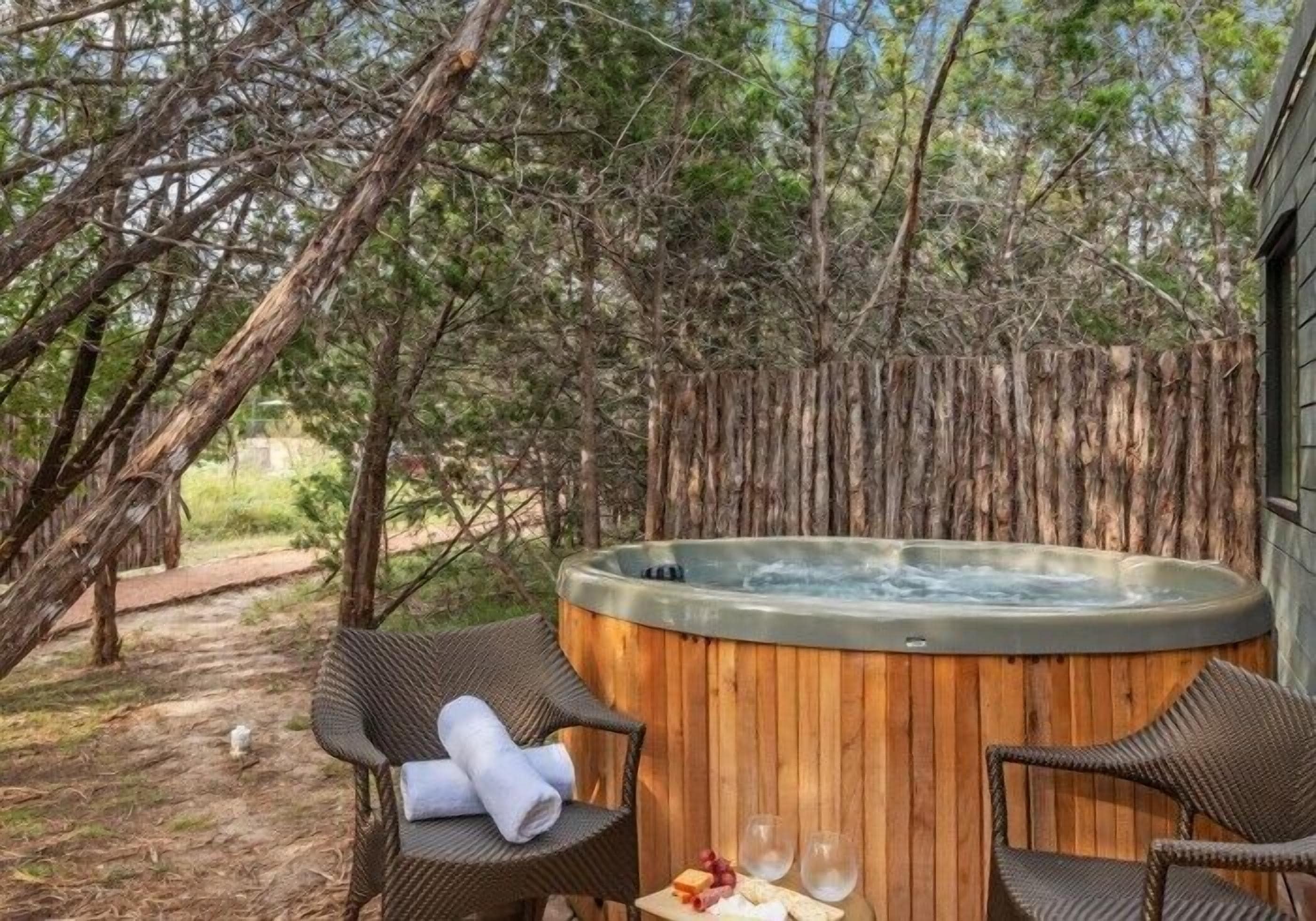 A hot tub surrounded by wicker chairs and a table with snacks and glasses.
