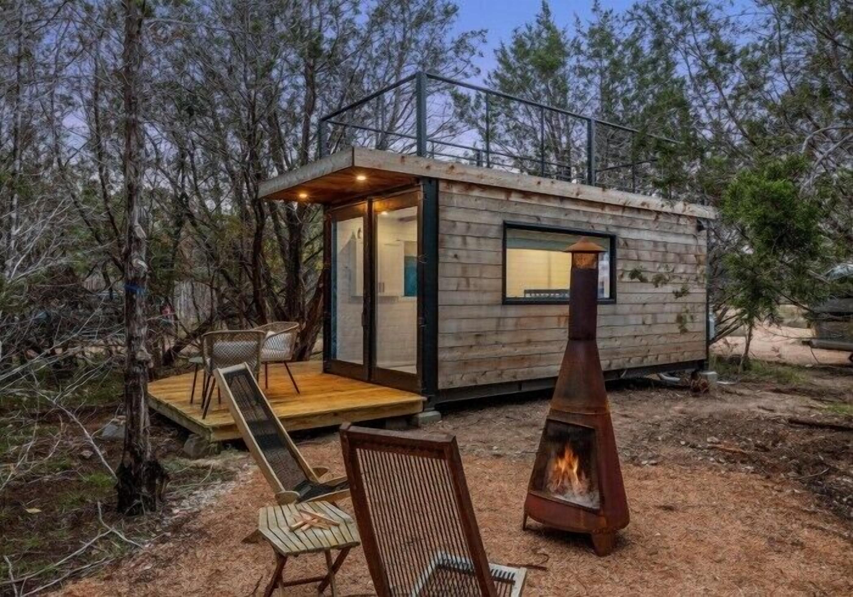 A small cabin with a wooden exterior, a deck with chairs, and a fire pit.