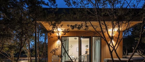 A modern wooden cabin with a deck, two wicker chairs, and a hot tub.