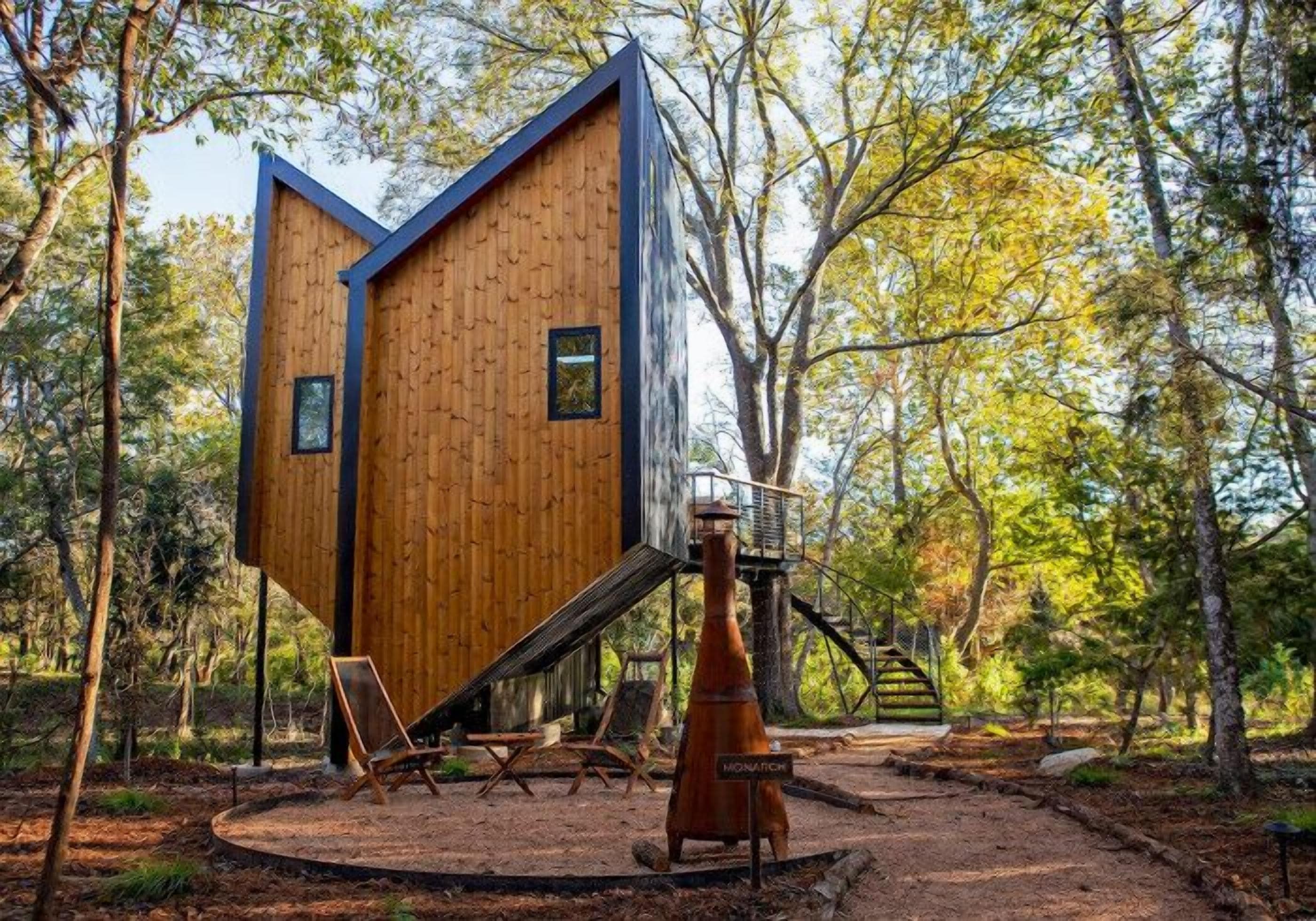 A modern wooden cabin with a unique triangular design, surrounded by a forest.