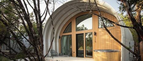 A modern, circular building with large windows and a wooden exterior, surrounded by trees and a grassy area.