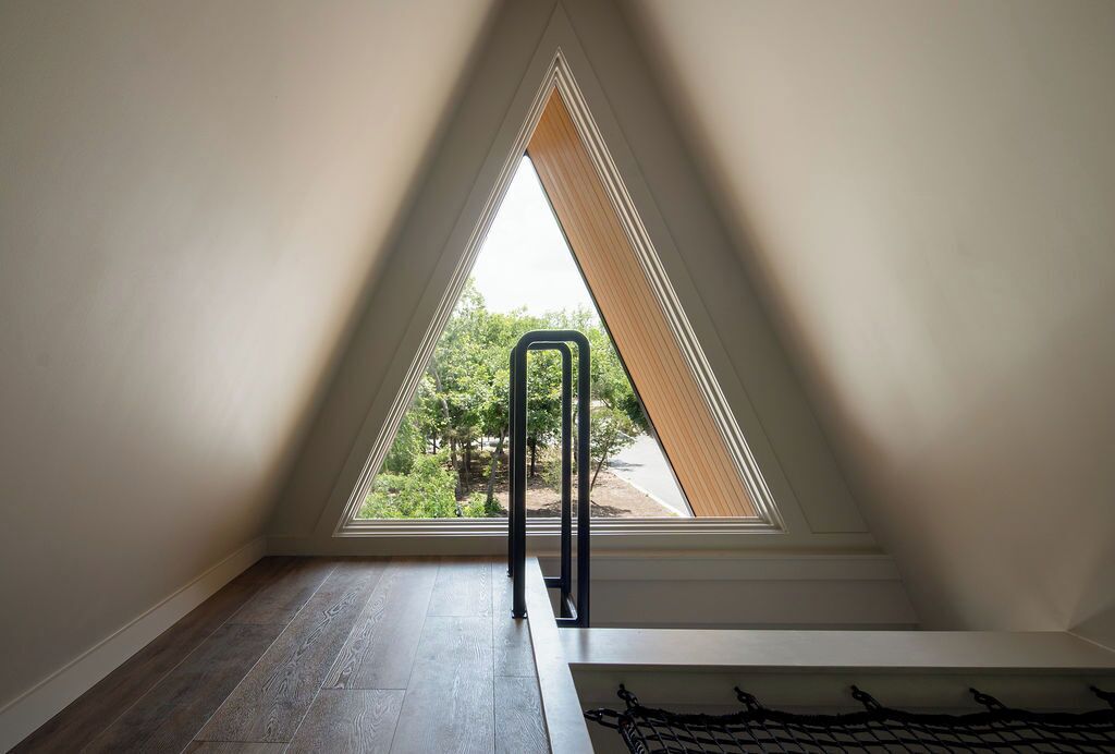 Une pièce mansardée triangulaire avec un puits de lumière, une échelle en métal et un plancher en bois.