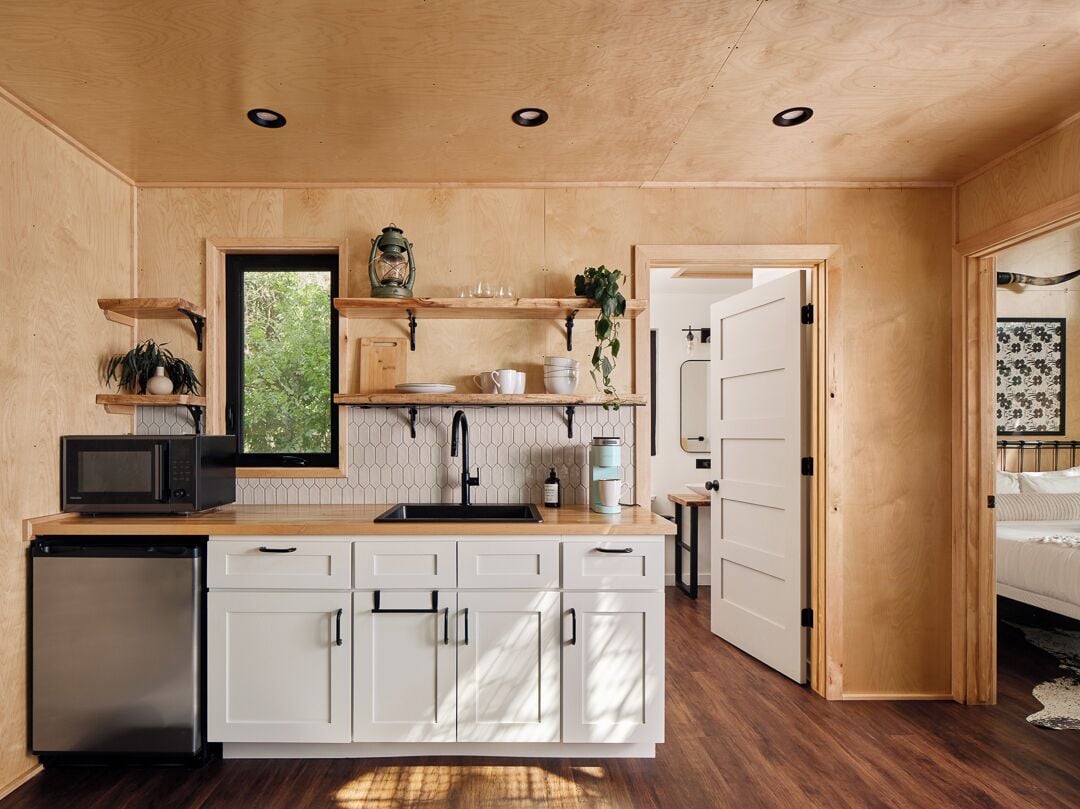Une cuisine compacte avec des meubles blancs, un four à micro-ondes et un évier. On y trouve un plan de travail en bois et un petit réfrigérateur.