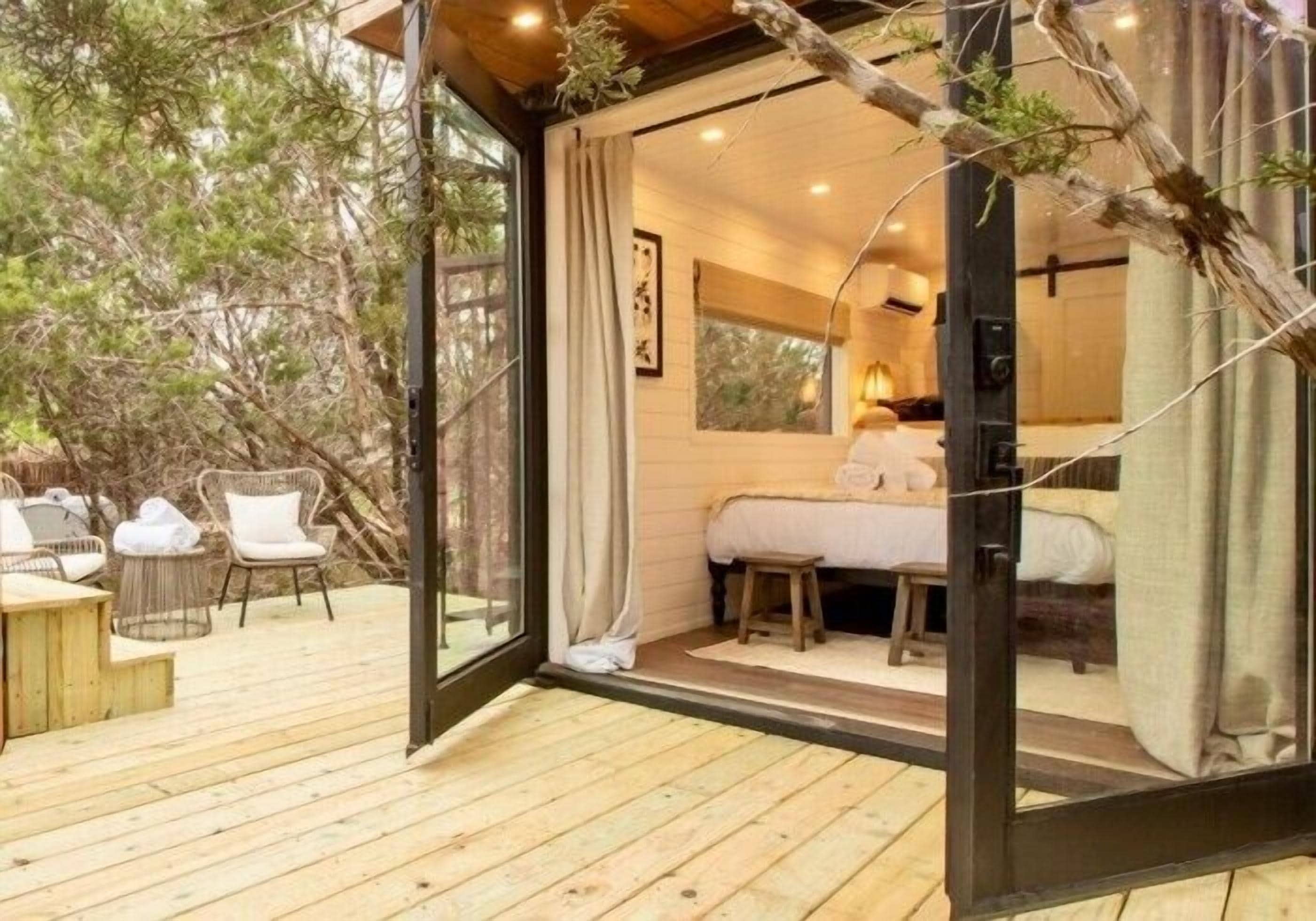 A cozy cabin with a wooden deck, a bed, and a small table with chairs.