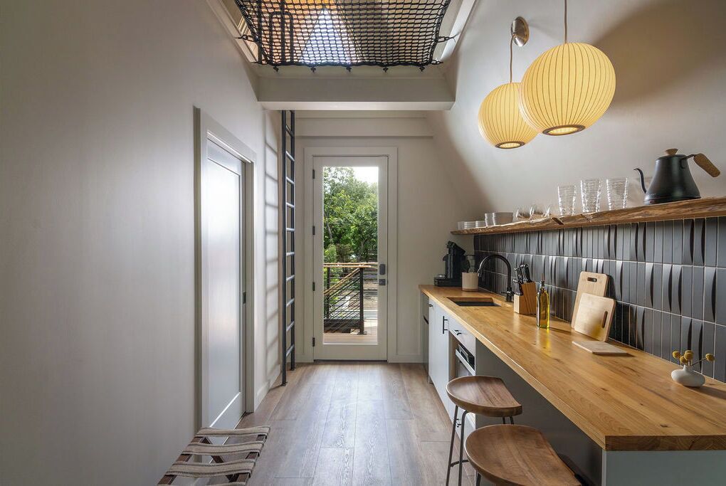 A modern kitchen with a wooden countertop, bar stools, and a view to the outside.