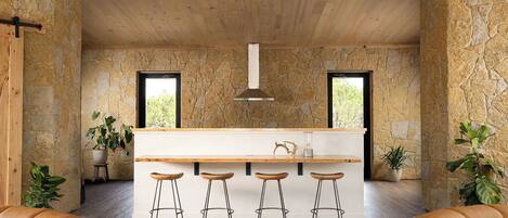 A modern kitchen with a central island, bar stools, and stone walls.