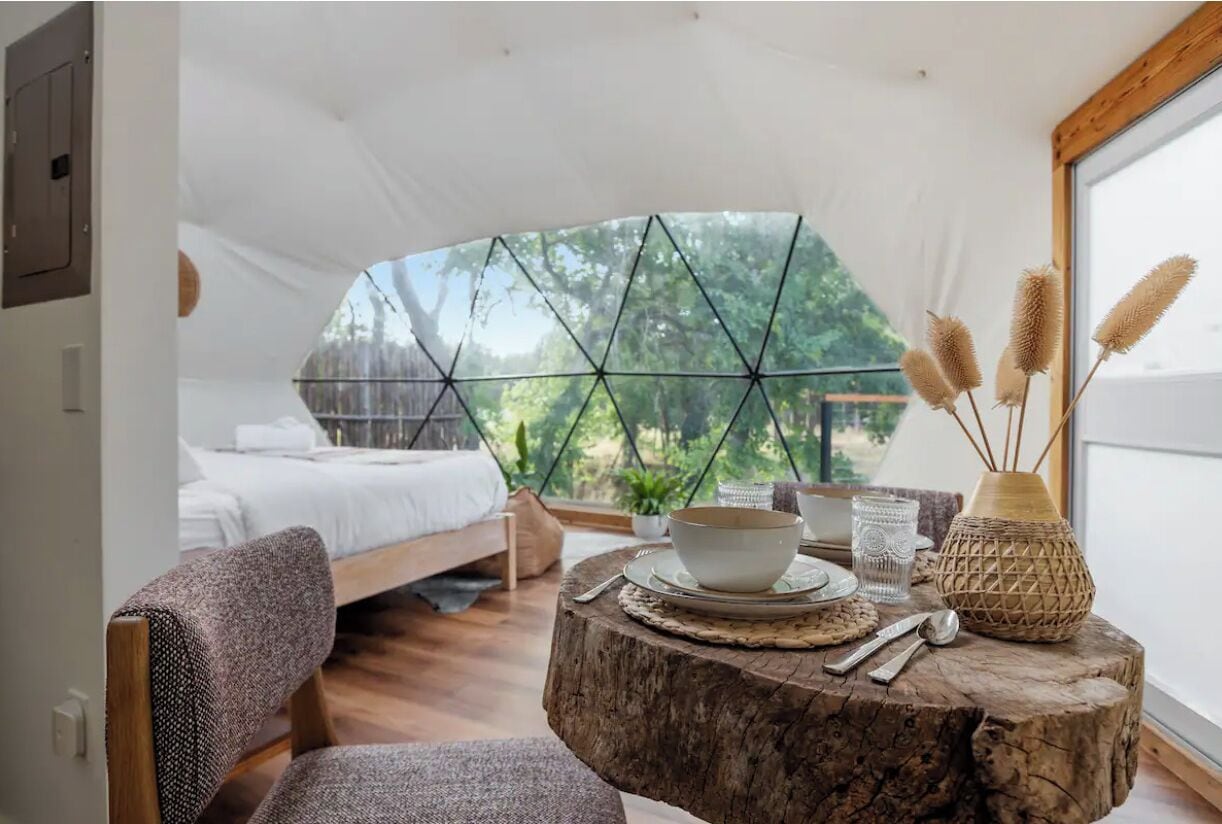 A cozy bedroom with a bed, a round wooden table with a bowl, a glass, and a decorative vase.
