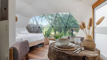 A cozy bedroom with a bed, a round wooden table with a bowl, a glass, and a decorative vase.