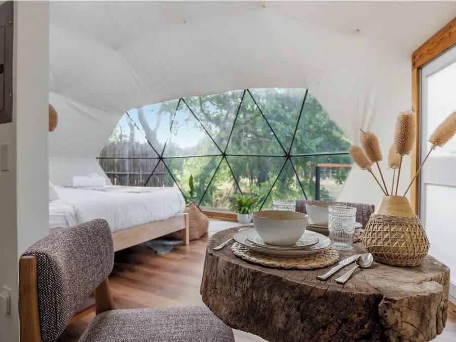 A cozy bedroom with a bed, a round wooden table with a bowl, a glass, and a decorative vase.