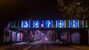 Un carrer sota un senyal amb la paraula "ACTON" il·luminada amb llums blaves.