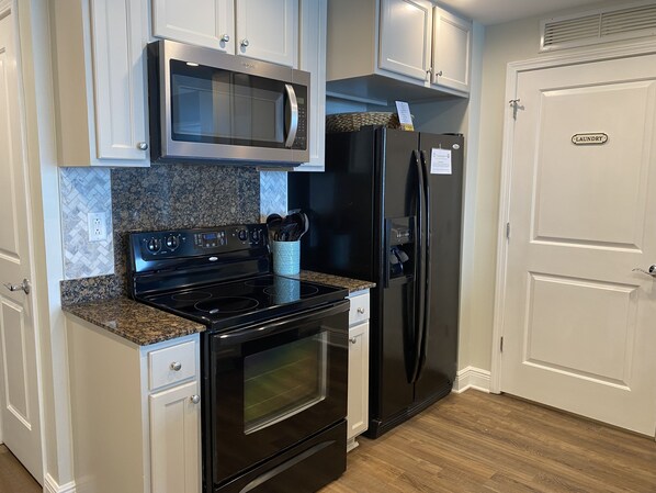 A kitchen with a stainless steel microwave, a black refrigerator, a stove, and a double oven. There is a granite countertop and white cabinetry.