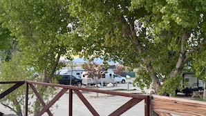 Un terrain de camping avec des camping-cars stationnés, une terrasse en bois et des arbres offrant de l’ombre.